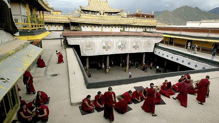 Zahlreiche Mönche in roten Gewändern im Innehof eines Kloster beim Debattieren.