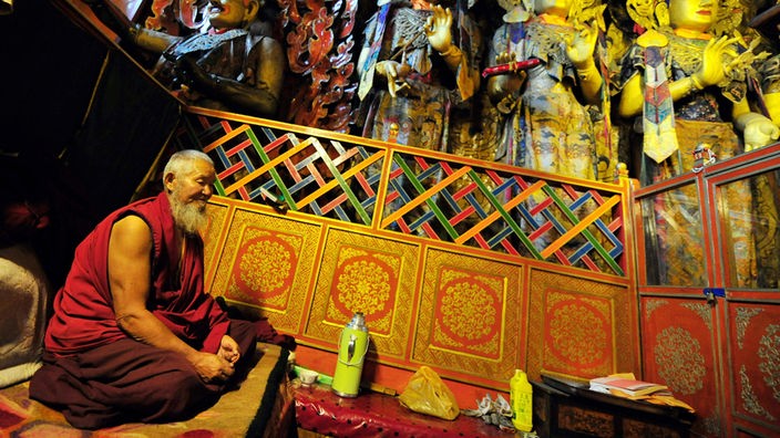 Ein alter Mönch meditiert im Inneren eines tibetischen Kloster.