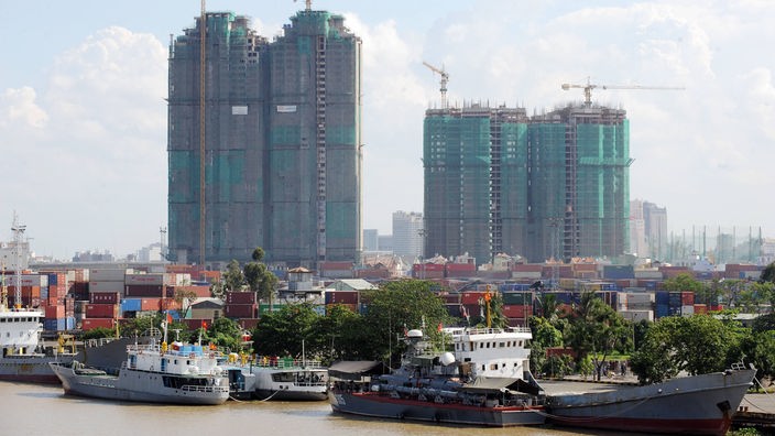 Blick auf den Hafen von Hanoi mit ein paar Schiffen im Vordergrund und zwei Hochhäusern im Rohbau im Hintergrund.