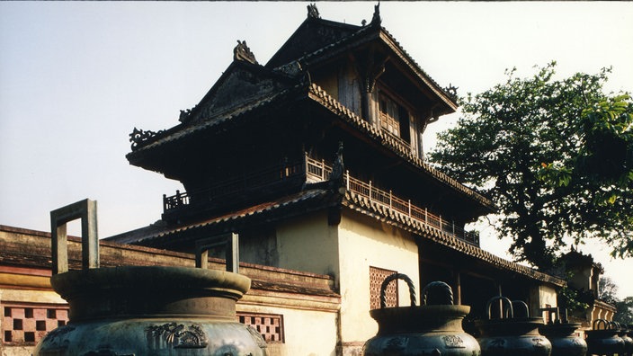 Blick auf ein Gebäude eines vietnamesischen Palastes. Davor ein großer kesselartiger Behälter. | Bildquelle: WDR/laif Blick auf ein Gebäude eines vietnamesischen Palastes. Davor ein großer kesselartiger Behälter.