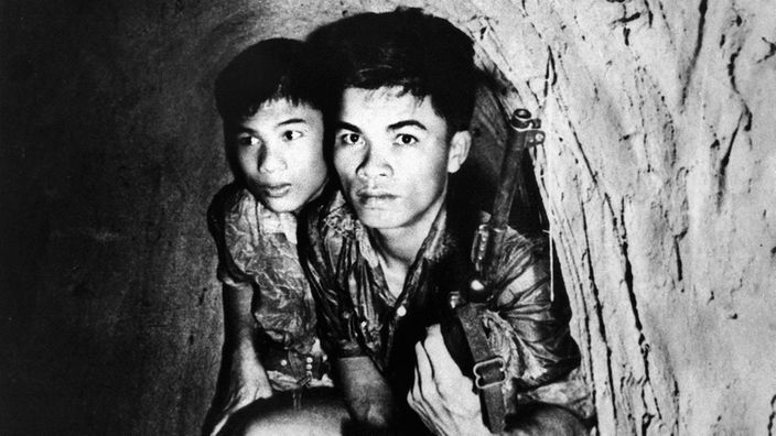 Das Schwarz-Weiß-Bild zeigt zwei junge bewaffnete Vietkong die geduckt durch einen Tunnel gehen.