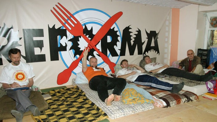 Lehrer und Eltern an einer russischen Schule in Riga protestierten mit einem Hungerstreik gegen Lettisch als verpflichtende Unterrichtssprache. Sie liegen auf Matratzen, im Hintergrund ein Spruchband mit der Aufschrift "Reforma".