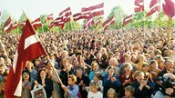 Eine Menschenmenge von vorne, lettische Flaggen schwenkend.