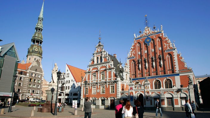Passanten auf dem kopfsteingepflasterten Rathausplatz vor dem Schwarzhäupterhaus und der St. Petrikirche in der Altstadt von Riga