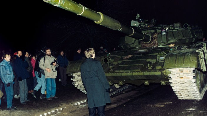 Ein Mann steht in der Dunkelheit unmittelbar vor einem Panzer.