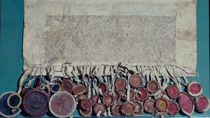 Handschriftlicher Text auf Pergamentpapier, daran sind viele Siegel befestigt.