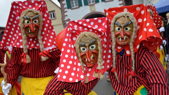Drei Frauen tragen zu Fasnacht rote Kostüme und die traditionellen Hexenmasken.