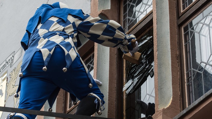 Ein verkleideter Fasnachts-Narr macht sich an der Scheibe des Rathaus zu schaffen | Bildquelle: dpa / Patrick Seeger Ein verkleideter Fasnachts-Narr macht sich an der Scheibe des Rathaus zu schaffen