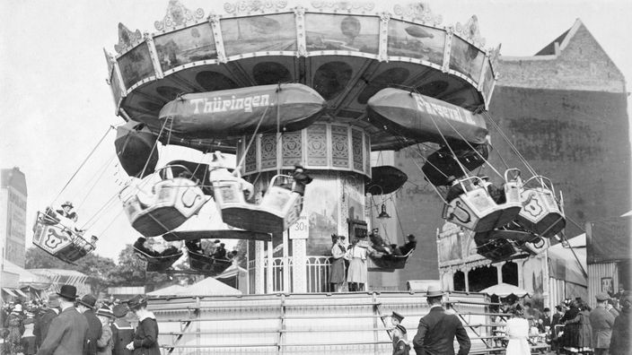 Ein Karussell Anfang des 20. Jahrhunderts: Die Fahrgäste sitzen in Gondeln, die mit Seilen befestigt sind