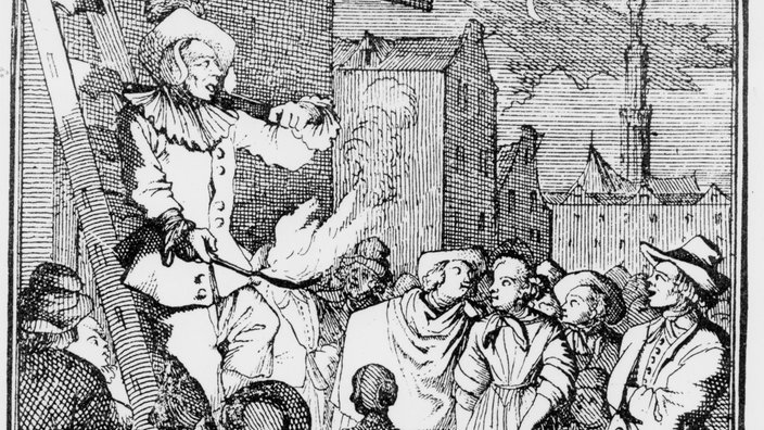 Ein Feuerschlucker steht auf einer Leiter, um ihn herum stehen Jahrmarktbesucher und sehen ihm zu | Bildquelle: akg Ein Feuerschlucker steht auf einer Leiter, um ihn herum stehen Jahrmarktbesucher und sehen ihm zu