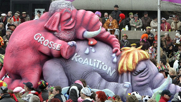 Wagen eines Umzuges: Auf zwei riesigen Elefanten aus Pappmaché steht 'Große Koalition'. Der rote hintere Elefant besteigt den grauen vorderen Elefanten.