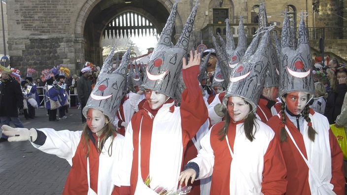 Beim Karnevalsumzug haben mehrere junge Mädchen Hüte auf dem Kopf, die den Kölner Dom darstellen sollen