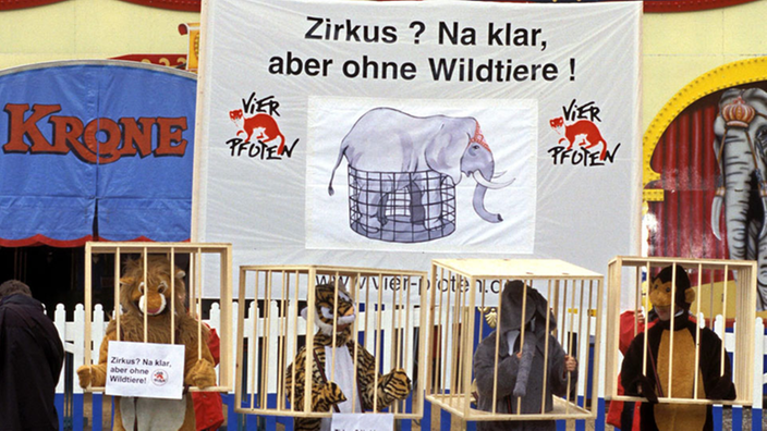 Menschen in Tierkostümen stehen vor Circus Krone. Im Hintergrund hängt ein Banner mit der Aufschrift: "Zirkus? Na klar, aber ohne Wildtiere!"