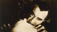 Filmszene aus dem Film "Wie schmeckt das Blut von Dracula?": Dracula beißt einer Frau, die der Kamera den Rücken zuwendet, in den Hals. Er trägt einen wahnsinnigen Gesichtsausdruck.