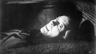 Schwarzweiß-Filmausschnitt: Hell geschminkter Kopf von Christopher Lee mit Blut triefendem Mund liegt Bild füllend im Dunklen
