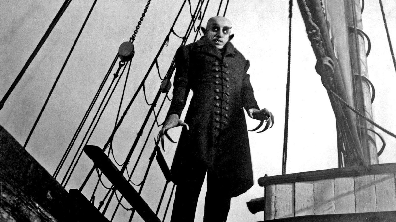 Schwarzweiße Filmszene: Dracula mit Glatze, schwarzem Mantel, großen Ohren und sehr langen Fingernägeln auf einem Schiff