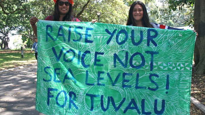 Zwei Frauen halten bei einer Demonstration zur Klimakonferenz 2015 ein Tuch mit der Aufschrift "Raise your voice not sea levels! For Tuvalu" in den Händen.