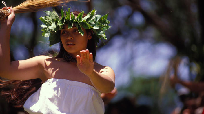 Auf Molokai tanzt eine Hawaiianerin in traditionellem Gewand und mit einem Blätterkranz auf dem Kopf den Hula.