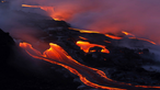 Dampfend fließen glühende Lavaströme durch das schwarze Gestein am Kilauea.