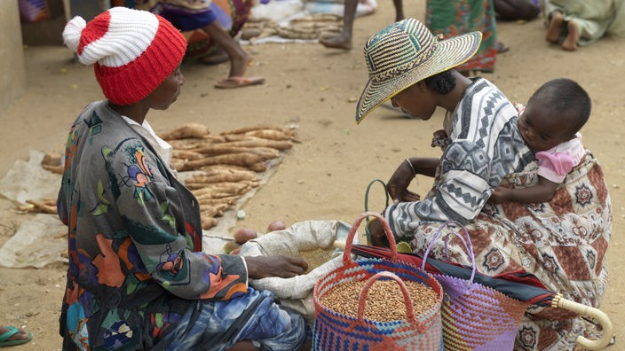 Frau mit Kind auf dem Rücken kauft auf traditionellem Markt ein