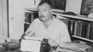 Schwarzweißfoto: Hemingway an seinem Schreibtisch mit Schreibmaschine.