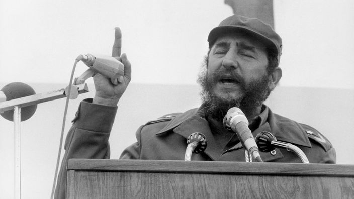 Fidel Castro steht 1976 an einem Pult mit Mikrophonen und hält eine Rede. Einen Finger reckt er mahnend in die Höhe