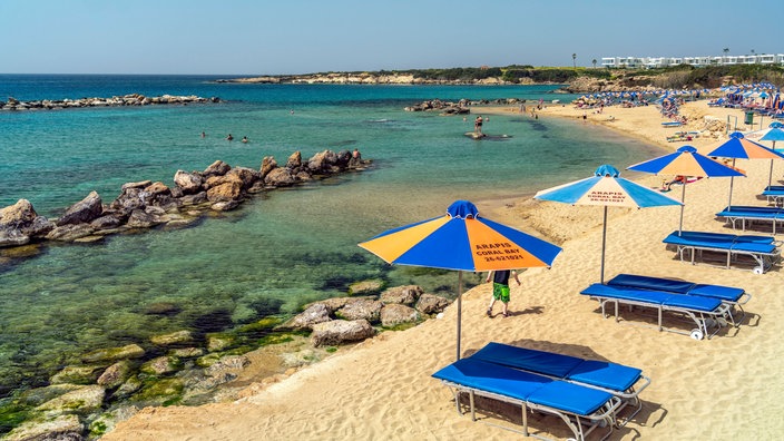 Ein Strand mit Sonnenschirmen und Liegen, im Hintergrund das Meer | Bildquelle: IMAGO/Peter Schickert Ein Strand mit Sonnenschirmen und Liegen, im Hintergrund das Meer