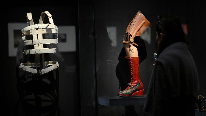 Der Besucher eines Museums schaut sich das Stahlkorsett und die Beinprothese Frida Kahlos an, die in einer Vitrine ausgestellt sind | Bildquelle: AFP / Emmanuel Dunand Der Besucher eines Museums schaut sich das Stahlkorsett und die Beinprothese Frida Kahlos an, die in einer Vitrine ausgestellt sind