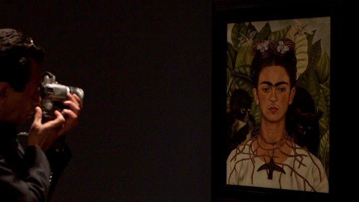 Der Besucher eines Museums macht ein Foto des Gemäldes “Selbstporträt mit Dornenkette und Kolibri“. Auf dem Gemälde ist Frida Kahlo zu sehen, die eine Dornenkette trägt, an der ein toter Kolibri hängt.