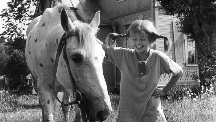 Pippi mit einem Schimmel auf einer Wiese vor ihrem Haus