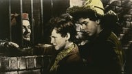 Filmszene: Tom Sawyer und Huckleberry Finn besuchen einen Gauner, der durch ein vergittertes Fenster zu den Jungen herausspäht