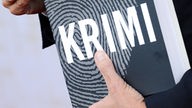 Mann hat ein Buch mit der Aufschrift "Krimi" unterm Arm