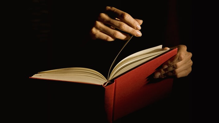 Eine Hand blättert eine Seite in einem roten Buch um