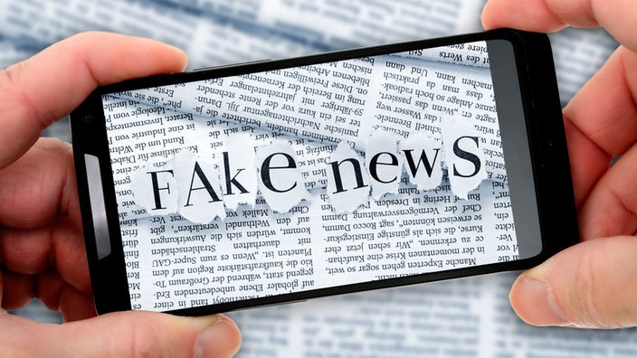 Handy, auf dem aus rausgerissenen Zeitungslettern "Fake News" steht
