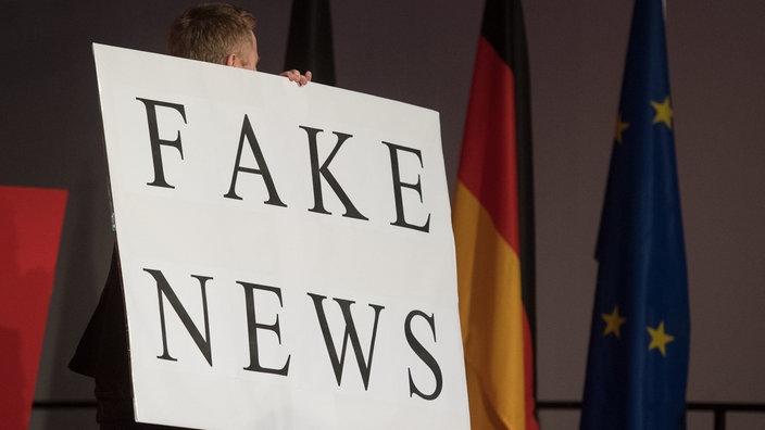 Ein Mann trägt beim politischen Aschermittwoch der baden-württembergischen CDU ein Schild mit der Aufschrift "Fake News" | Bildquelle: dpa/Marijan Murat Ein Mann trägt beim politischen Aschermittwoch der baden-württembergischen CDU ein Schild mit der Aufschrift "Fake News"