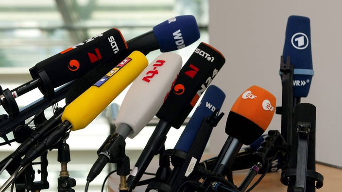 Die Mikrofone verschiedener deutscher Fernsehsender stehen für eine Pressekonferenz bereit.
