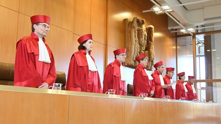 Die Richter des Bundesverfassungsgerichts stehen in ihren roten Roben am Richtertisch.