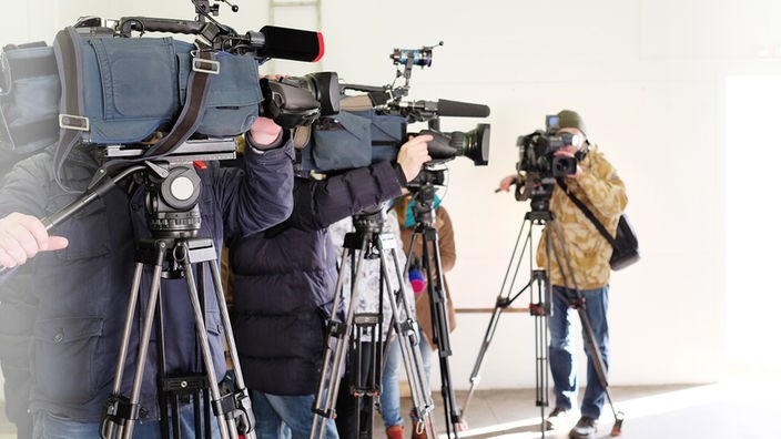 Filmkameras stehen mit Journalisten in einer Reihe.
