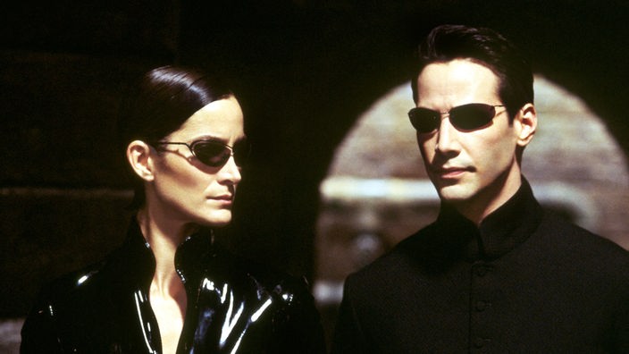 Filmszene aus 'Matrix Reloaded': Die Schauspieler Keanu Reeves und Carrie-Anne Moss mit schwarzer Kleidung und dunklen Sonnenbrillen.