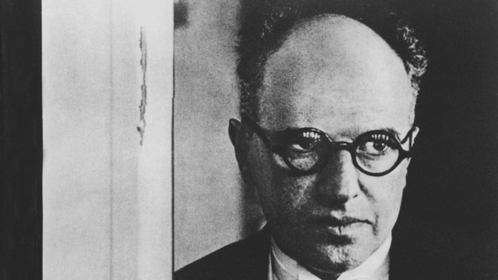 Erich Salomon lehnt an einer Tür, hat eine Kamera in der Hand und schaut den Fotografen an | Bildquelle: akg Erich Salomon lehnt an einer Tür, hat eine Kamera in der Hand und schaut den Fotografen an