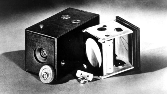 Das schwarz-weiß Foto zeigt die erste Kodak-Kamera. Rechts daneben liegt die Halterung für den Rollfilm, die in die Kamera eingeschoben wurde. | Bildquelle: Kodak Das schwarz-weiß Foto zeigt die erste Kodak-Kamera. Rechts daneben liegt die Halterung für den Rollfilm, die in die Kamera eingeschoben wurde.