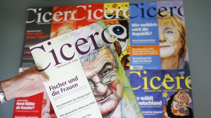 Zwei Hände halten eine Ausgabe des Magazins 'Cicero' in die Kamera, auf dem eine Zeichnung von Joschka Fischer zu sehen ist. Im Hintergrund liegen weitere 'Cicero'-Ausgaben.