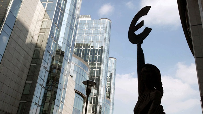 Die dunkle Silhouette des Euro-Symbols ragt vor den hellen Glasfronten des Europaparlaments auf. | Bildquelle: dpa/Lehtikuva Die dunkle Silhouette des Euro-Symbols ragt vor den hellen Glasfronten des Europaparlaments auf.