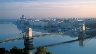 Blick auf eine Brücke und Häuser am Donauufer in Budapest.