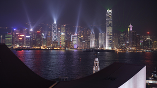Blick auf die bunt erleuchteten Hochhäuser der Skyline von Hongkong bei Nacht.