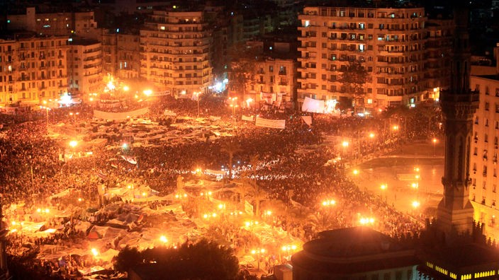 Nachtaufnahme eines großen Platzes gefüllt mit Demonstranten, ringsherum Hochhäuser