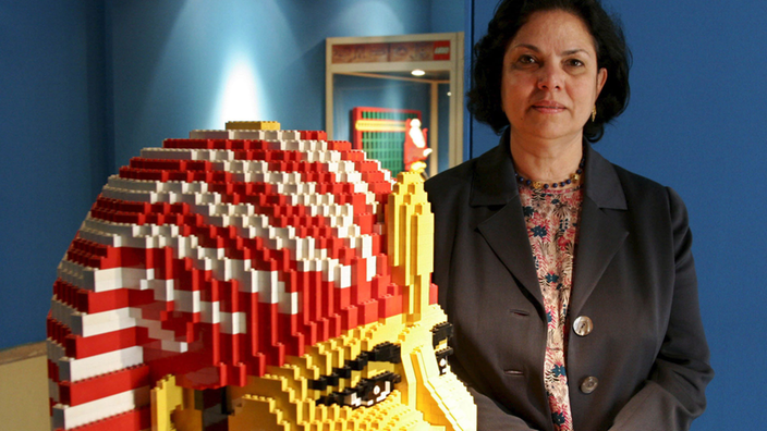 Schwarzhaarige Frau steht neben einer großen Büste eines Pharaos, die aus Legosteinen besteht.