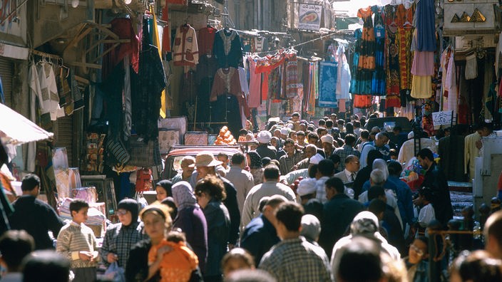 Ein Basar in der Altstadt von Kairo. Viele Menschen drängen sich durch die enge Straße, links und rechts kleine Läden.