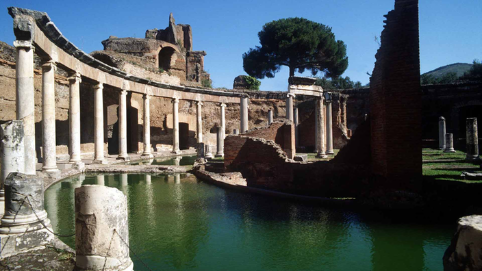 Für den Betrachter sichtbar ist ein halbrunder Säulengang, der einen halbrunden Wassergraben umschließt. Rechts im Bild: Ruinen auf einer kleinen Insel.