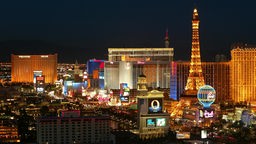 Bunt beleuchtete Silhouette von Las Vegas. Im Vordergrund ein Gebäude, das dem Pariser Eiffelturm nachempfunden ist.